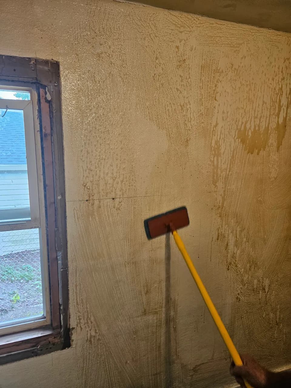 Extension-pad cleaning on a wall with brown residue beside a window